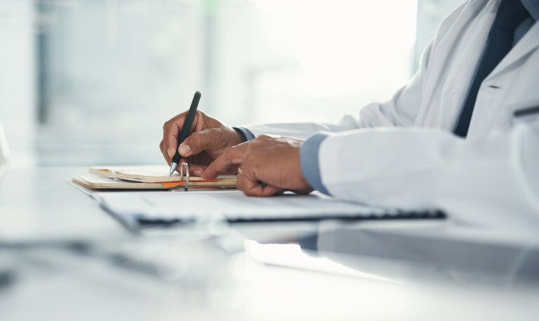 Doctor hands writing on paper or document at a desk in the hospital.